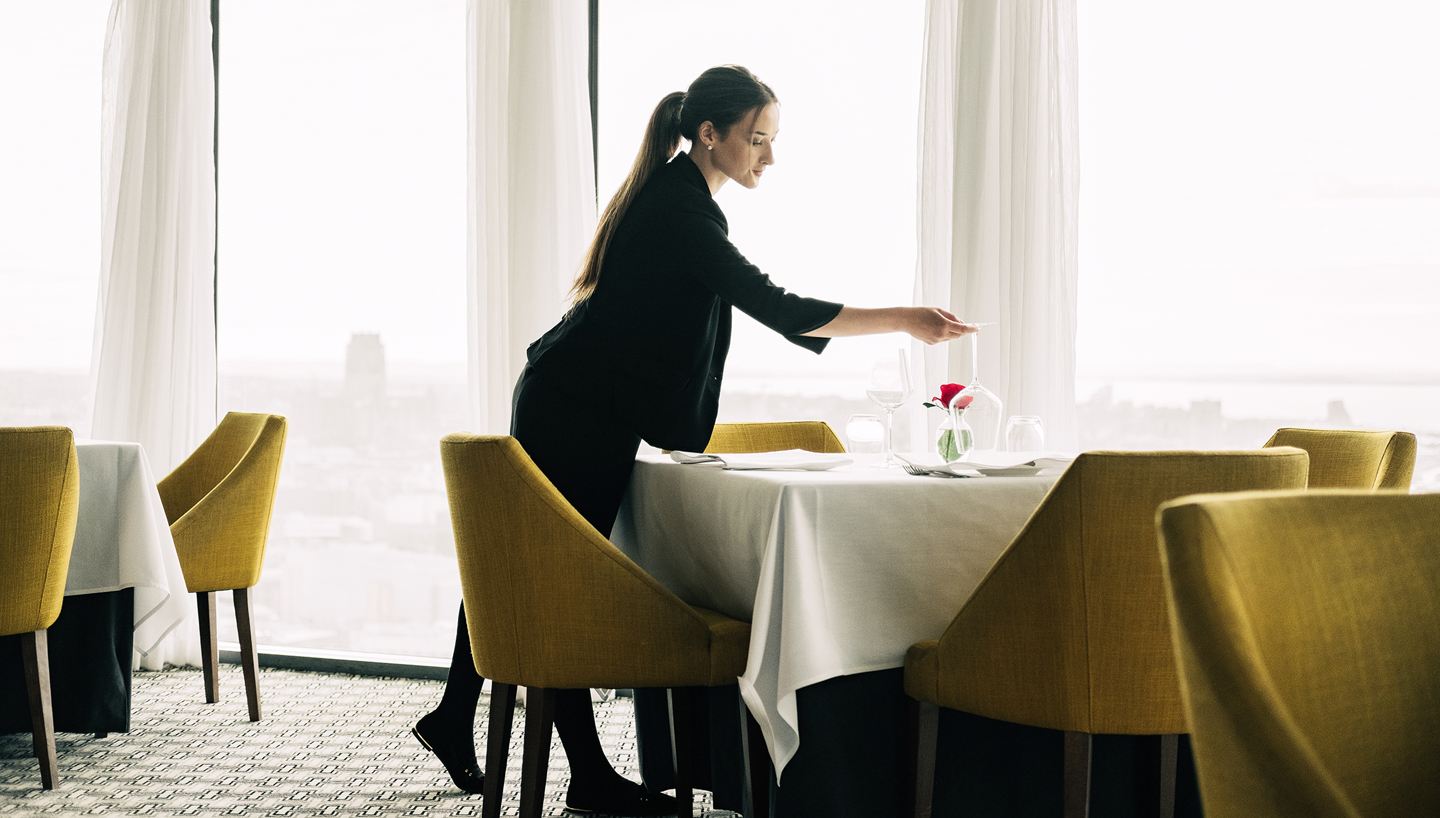 Waitress putting cutlery on a table in restaurant