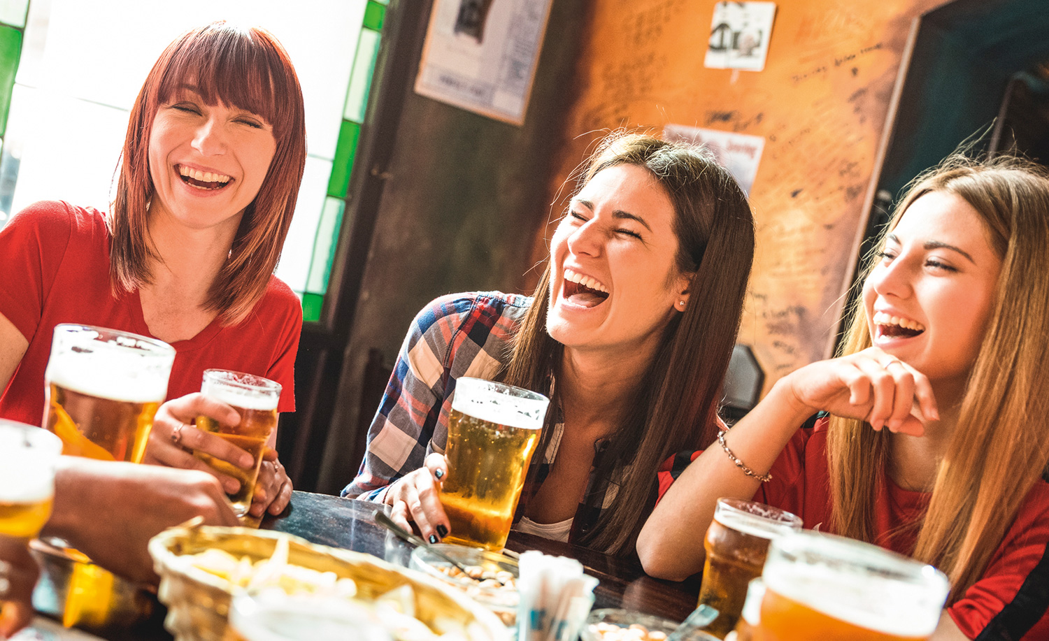 Three women laughing in a pub with drinks