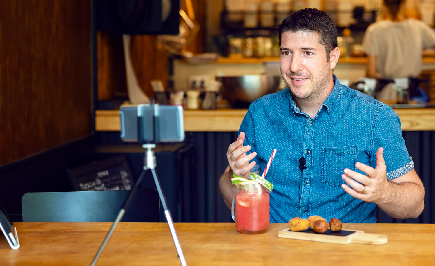 Man with drink on table talking to a phone camera