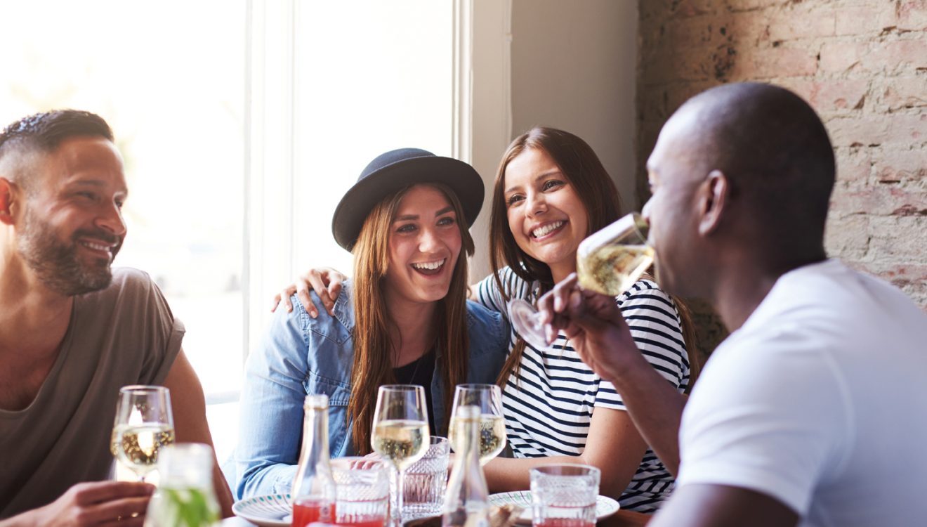 A group of friends enjoying a glass of wine laughing in a pub